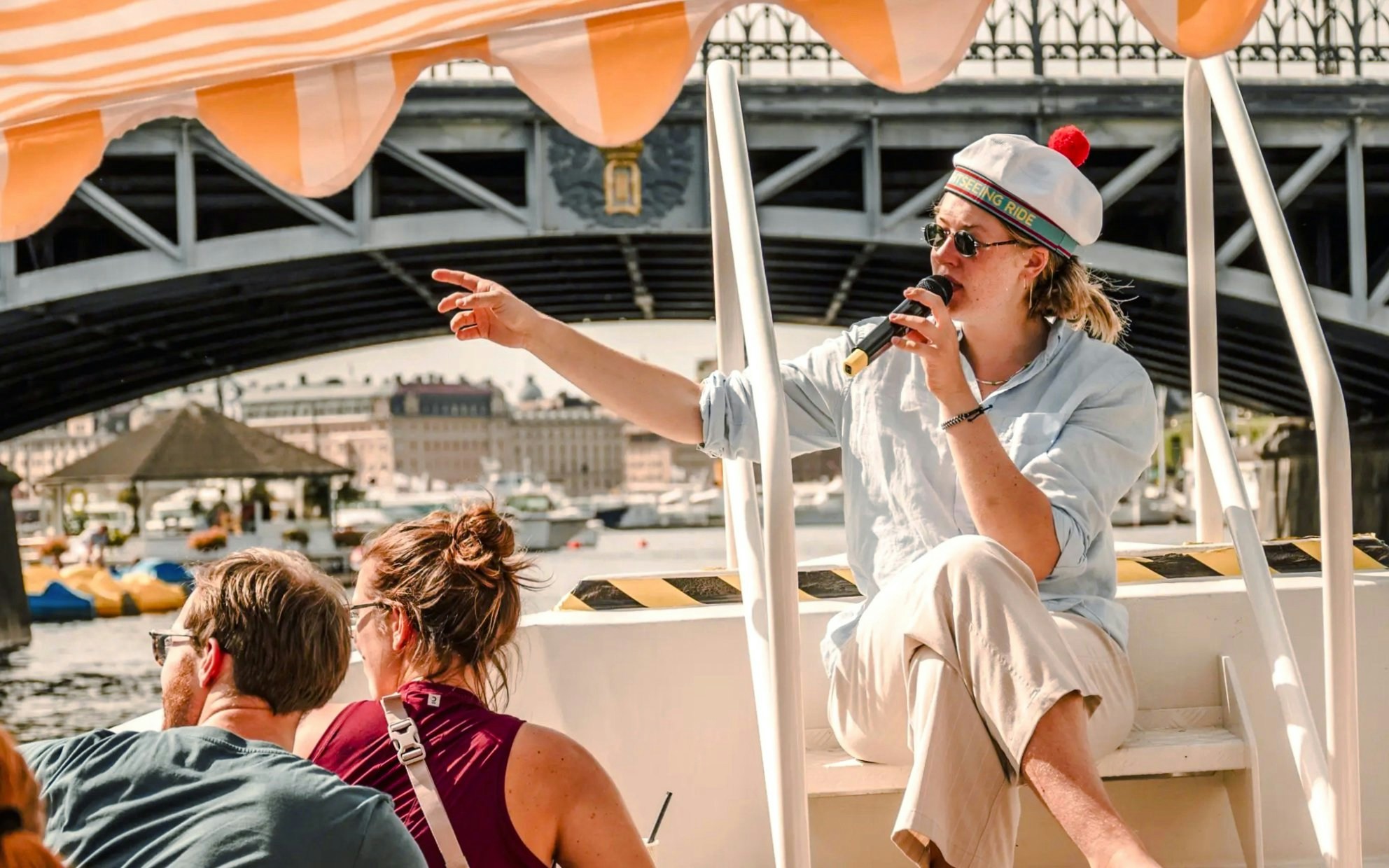 Guide narrating on a sightseeing boat tour in Stockholm under a bridge.