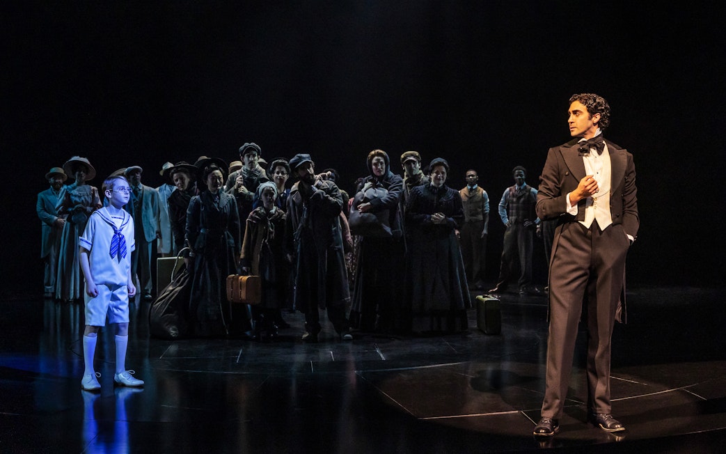 Actors on stage during a scene from the musical Ragtime, featuring a boy and a man in formal attire.