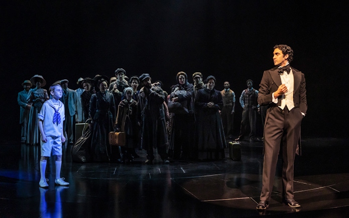 Actors on stage during a scene from the musical Ragtime, featuring a boy and a man in formal attire.