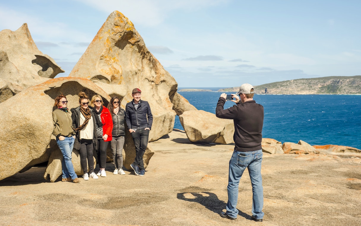 Man photographing group at Remarkable Rocks, Kangaroo Island with ocean backdrop.