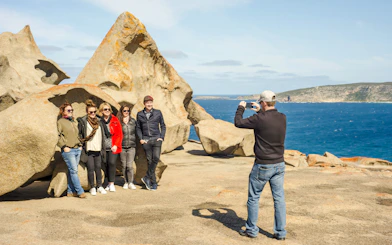 Man photographing group at Remarkable Rocks, Kangaroo Island with ocean backdrop.