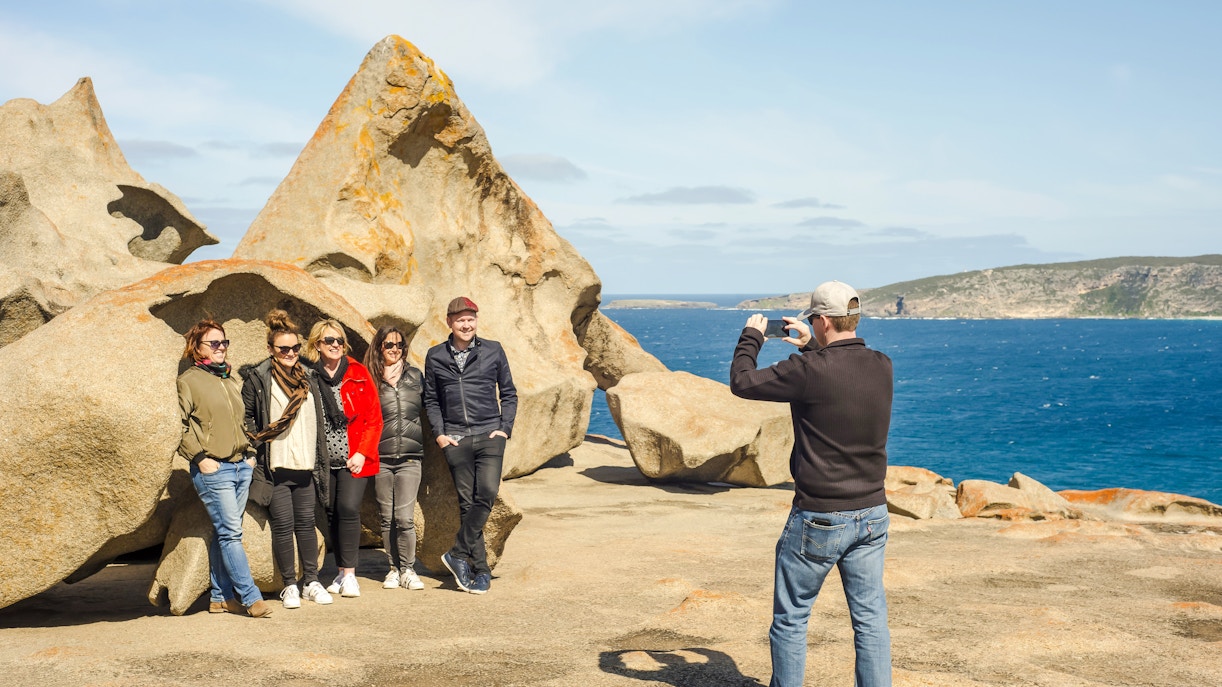 Man photographing group at Remarkable Rocks, Kangaroo Island with ocean backdrop.