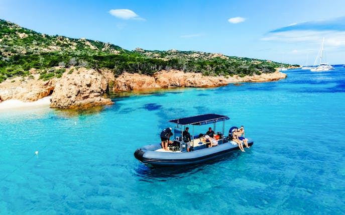 RIB boat with tourists exploring La Maddalena Archipelago's clear waters and rocky coastline.