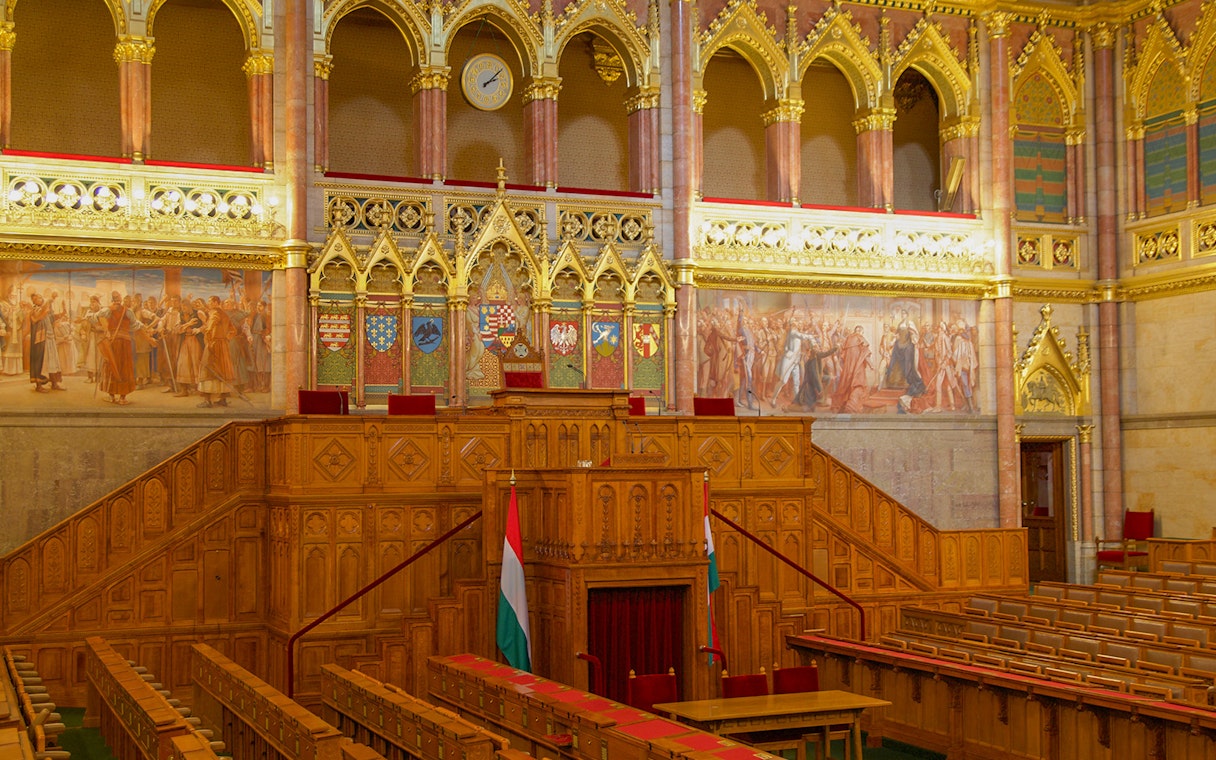 Hungarian Parliament meeting room with ornate woodwork and historical murals.