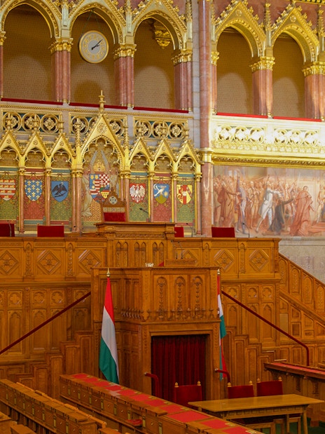 Hungarian Parliament meeting room with ornate woodwork and historical murals.