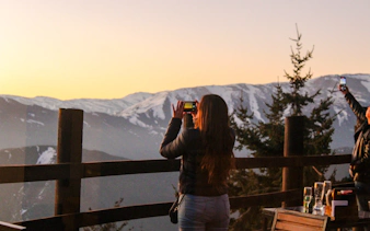 Tourists photographing sunset over Andes Mountains from Santiago viewpoint.