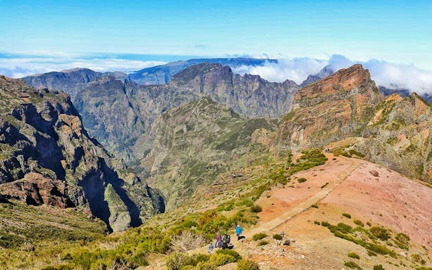 Hikers on a trail at Areiro Peak with views of Nun's Valley, Madeira.