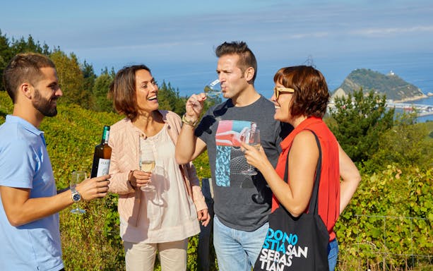Group enjoying wine tasting in Getaria vineyard with ocean view on Txakoli tour from San Sebastian.