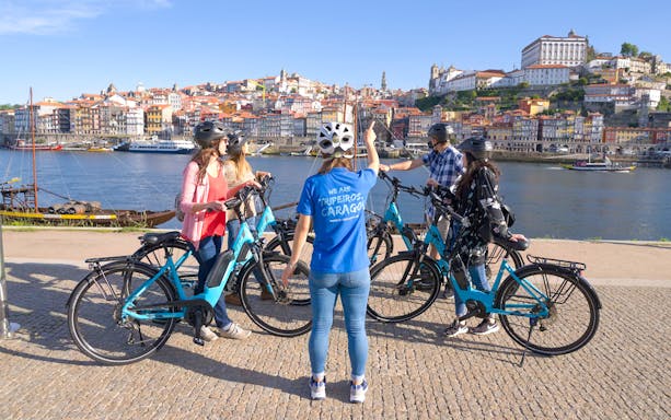 Group on electric bikes with guide by Douro River, Porto cityscape in background.