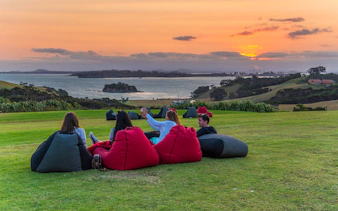 Friends relaxing on bean bags at Cable Bay Vineyard, enjoying wine with a sunset view.