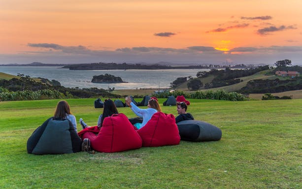 Friends relaxing on bean bags at Cable Bay Vineyard, enjoying wine with a sunset view.