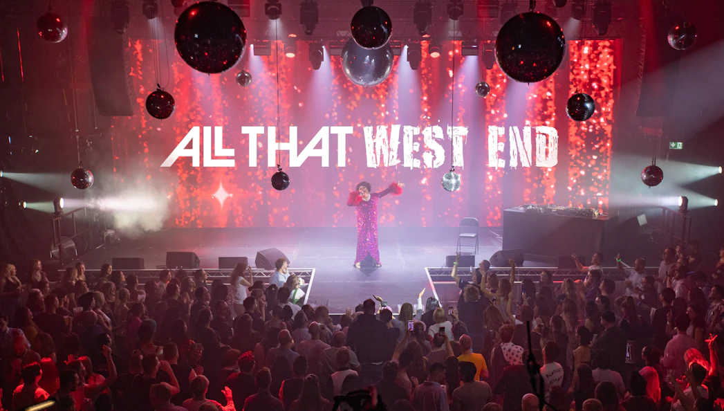 Performer on stage at "ALL THAT West End" show with audience in a vibrant theater setting.