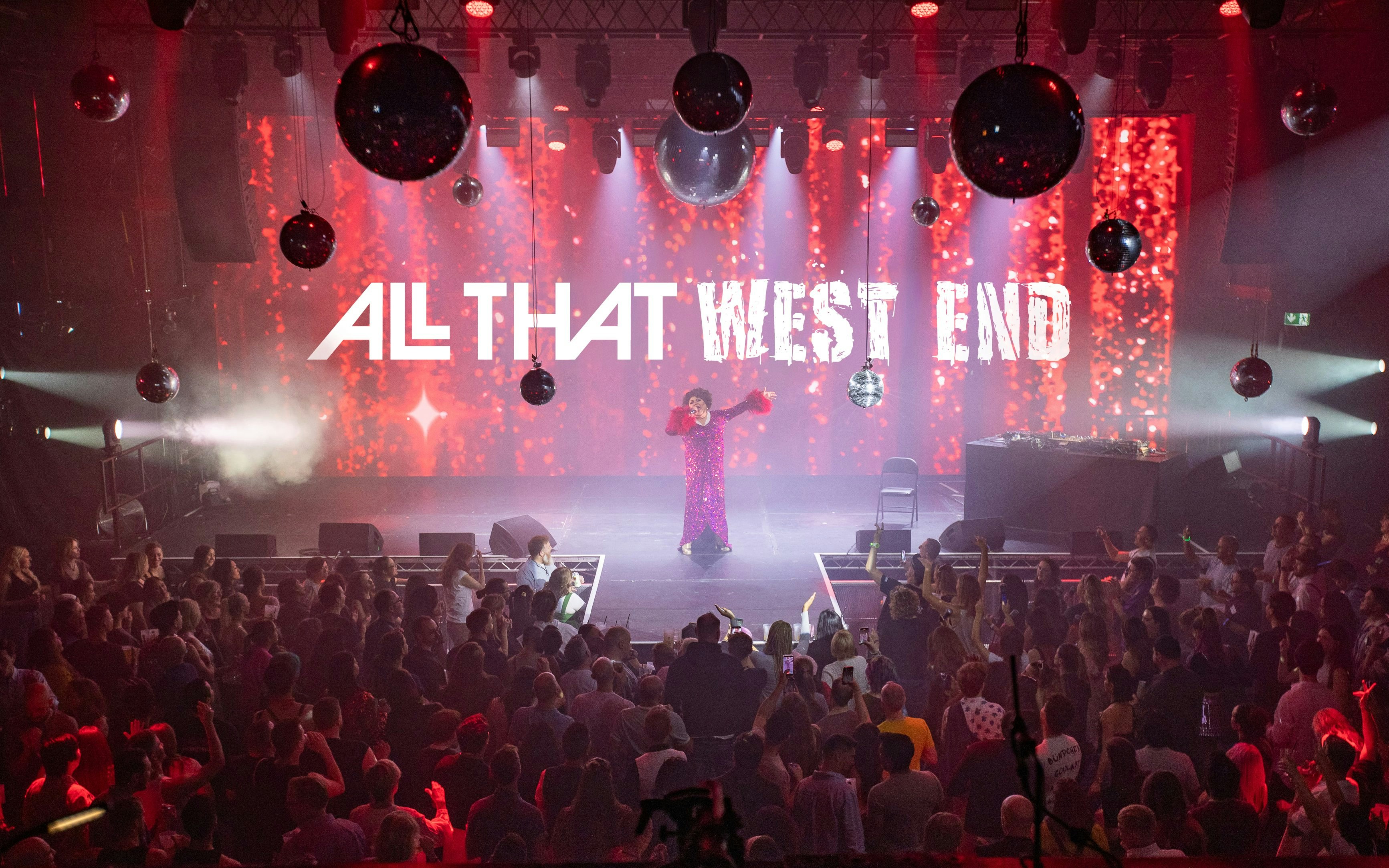 Performer on stage at "ALL THAT West End" show with audience in a vibrant theater setting.