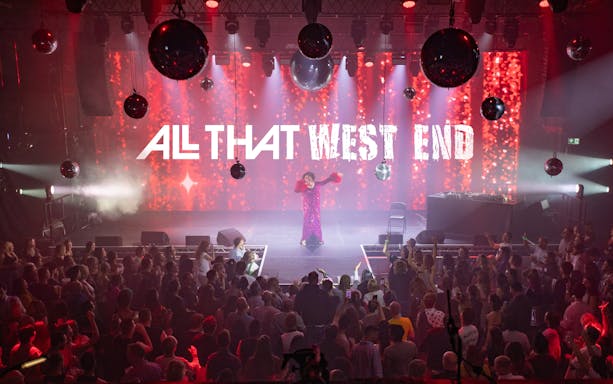 Performer on stage at "ALL THAT West End" show with audience in a vibrant theater setting.