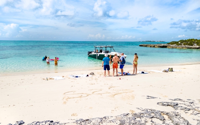 Tourists on Rose Island beach preparing to swim with pigs in clear turquoise water.