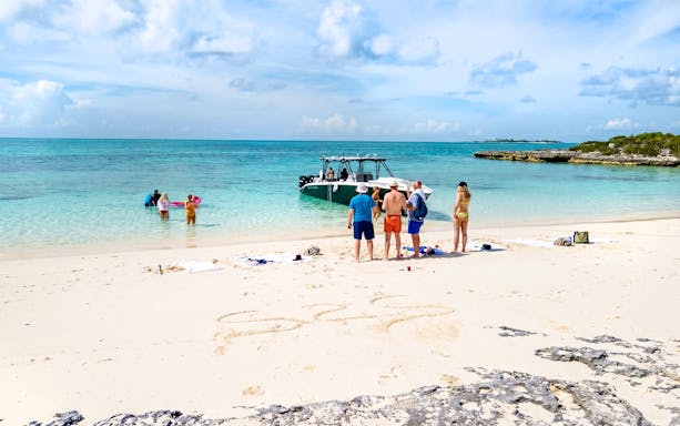 Tourists on Rose Island beach preparing to swim with pigs in clear turquoise water.