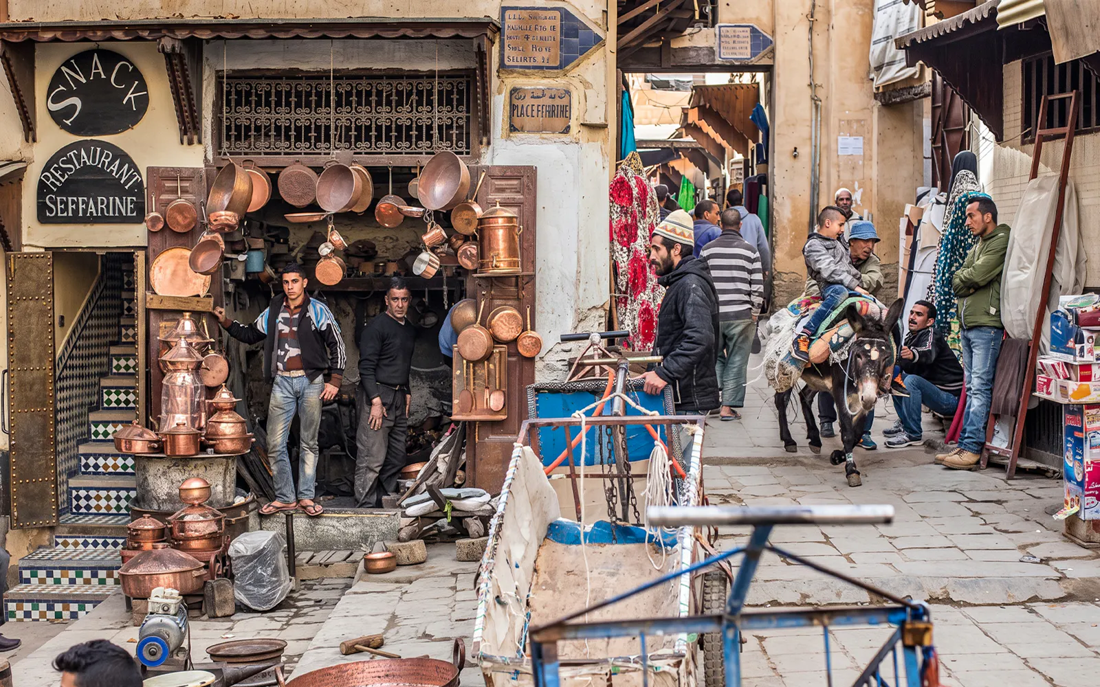 Fes Medina street scene with copper shop and people on a donkey during Chouara Tannery tour.