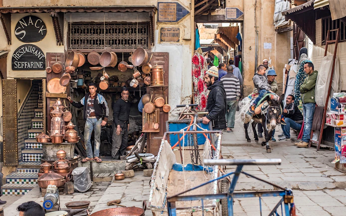 Fes Medina street scene with copper shop and people on a donkey during Chouara Tannery tour.