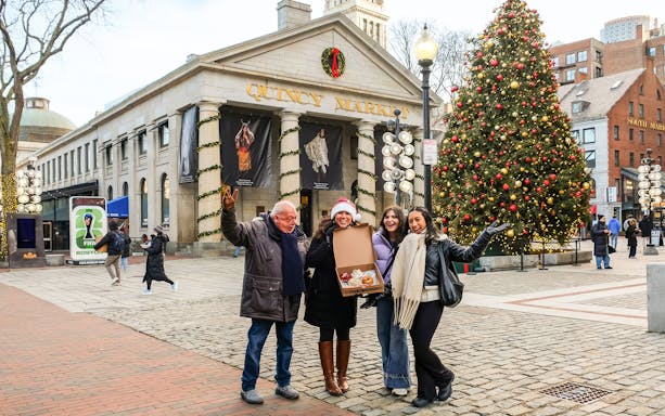 Group enjoying donut tour at Quincy Market, Boston, with a festive Christmas tree in the background.