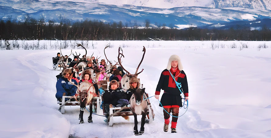 Reindeer sledding with Sami guide in snowy landscape, showcasing Sami culture.
