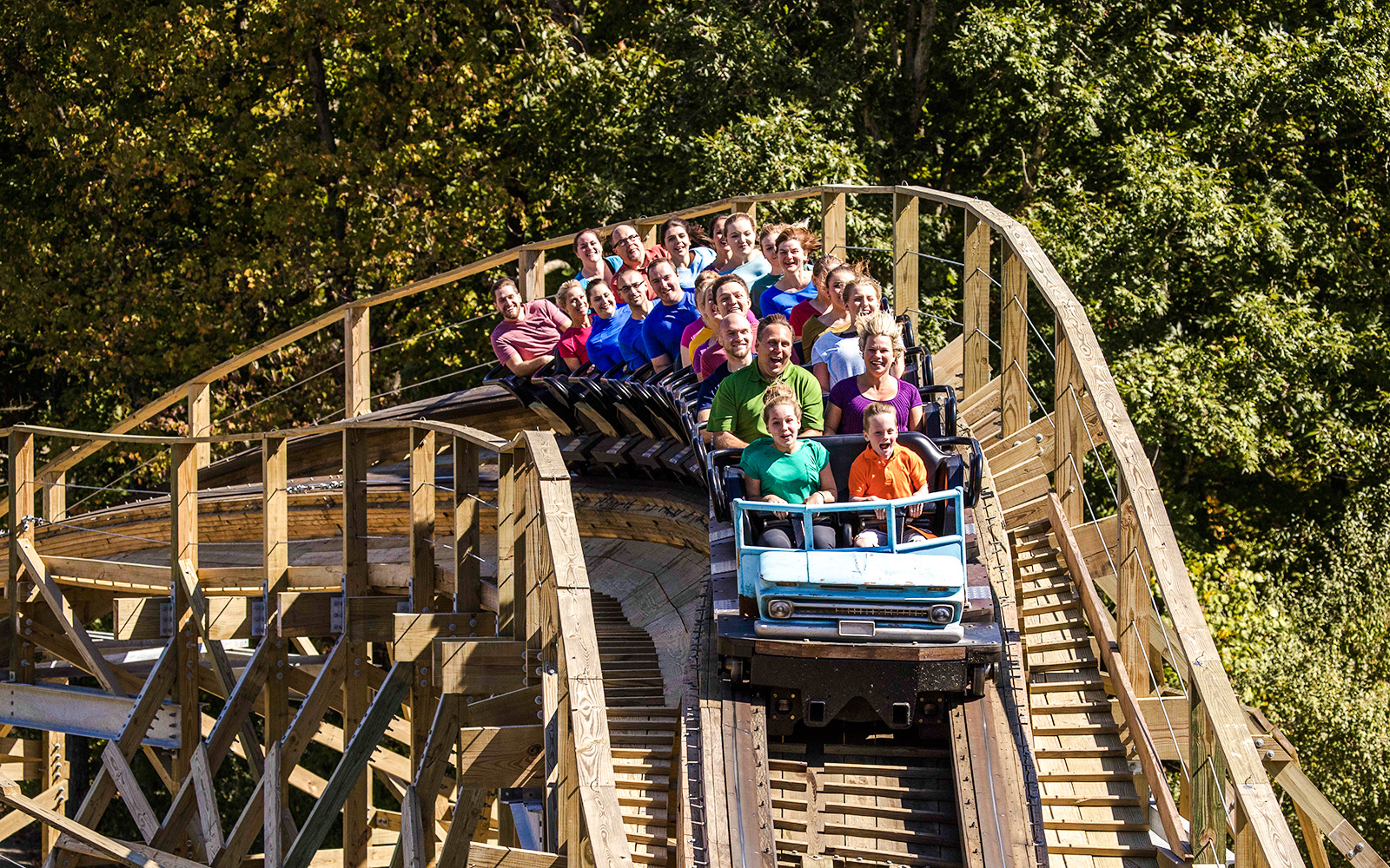 Riders on Mystic Timbers roller coaster at Kings Island, surrounded by trees.
