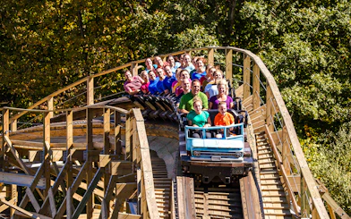 Riders on Mystic Timbers roller coaster at Kings Island, surrounded by trees.