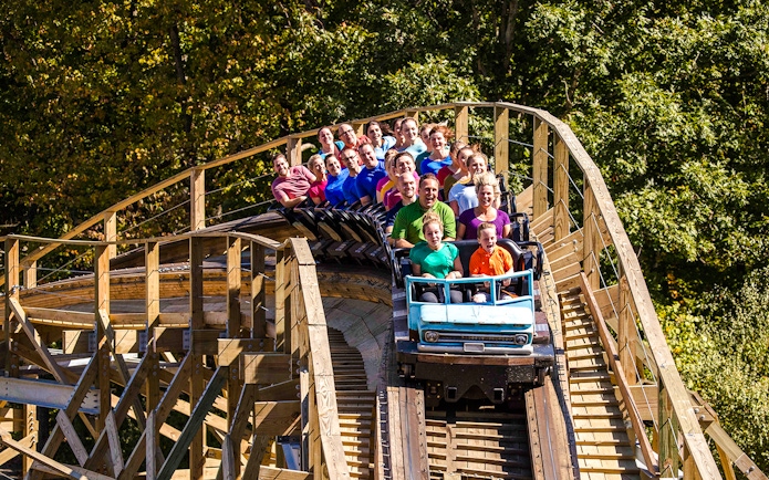Riders on Mystic Timbers roller coaster at Kings Island, surrounded by trees.
