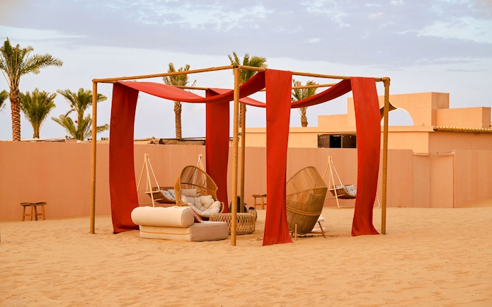 Lounge area with wicker chairs and red drapes at Noble Camp Desert Safari.
