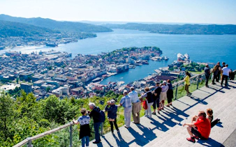 Tourists enjoying the view of Bergen, Norway, from Mount Fløyen's scenic viewpoint.