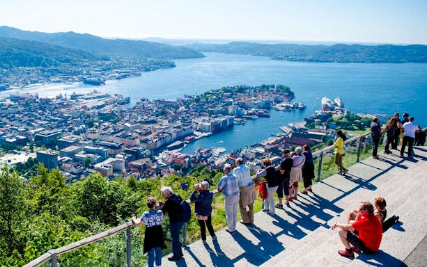 Tourists enjoying the view of Bergen, Norway, from Mount Fløyen's scenic viewpoint.