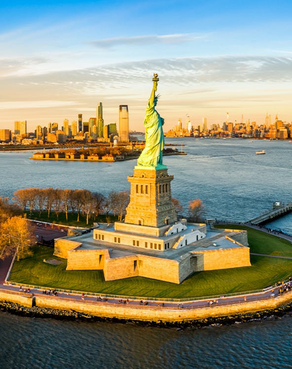 Aerial view of the Statue of Liberty with New York City skyline in the background.