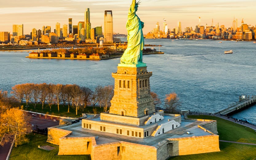 Aerial view of the Statue of Liberty with New York City skyline in the background.