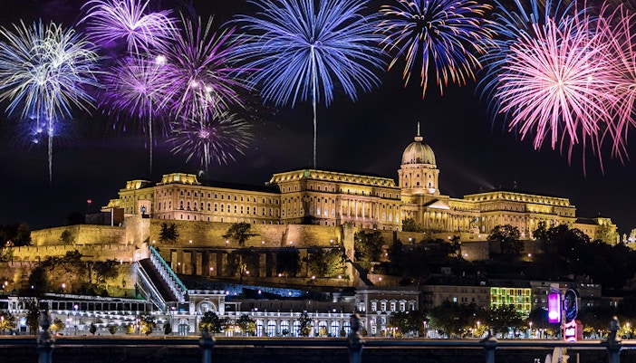 Budapest Castle illuminated at night with colorful fireworks in the sky.