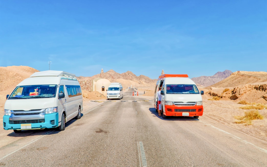 Vans on road to Ras Mohamed National Park, Egypt, with desert landscape.