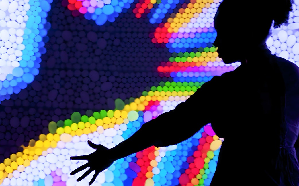 Silhouette of a person reaching towards colorful light display at the Exploratorium.