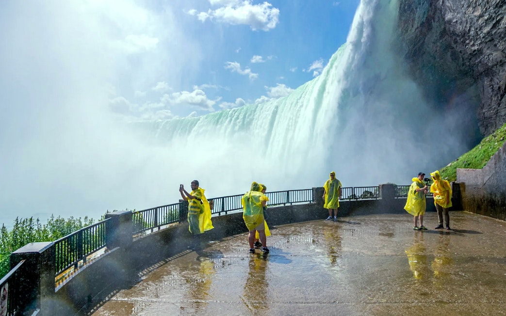 Visitors in yellow ponchos at Niagara Falls viewpoint, capturing the waterfall.