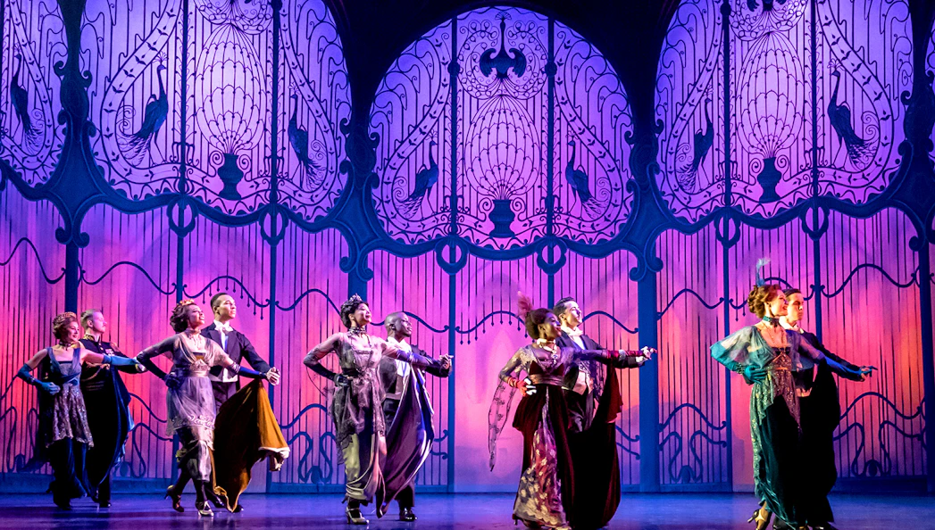 Performers dancing on stage in a scene from "My Fair Lady" with ornate backdrop.