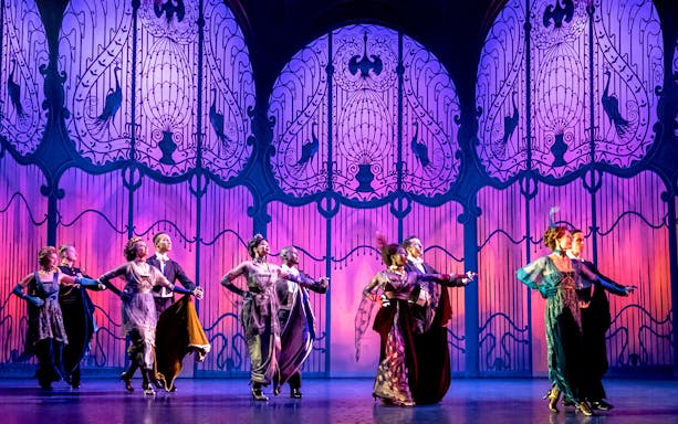 Performers dancing on stage in a scene from "My Fair Lady" with ornate backdrop.