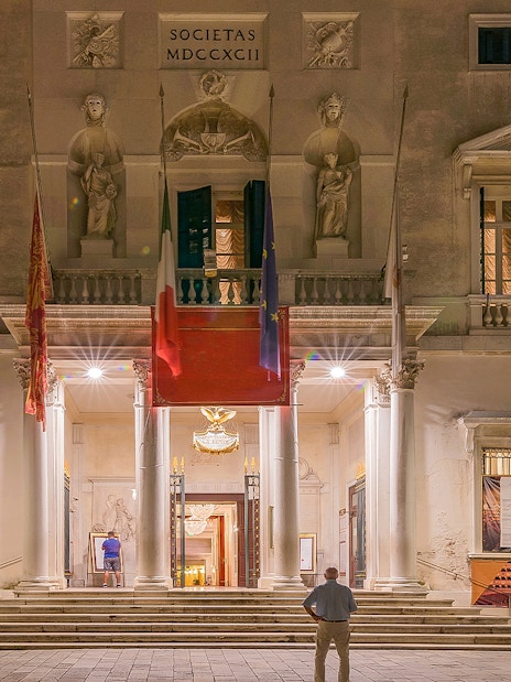 Facade of Fenice Theater in Venice at night, featuring illuminated entrance and architectural details.