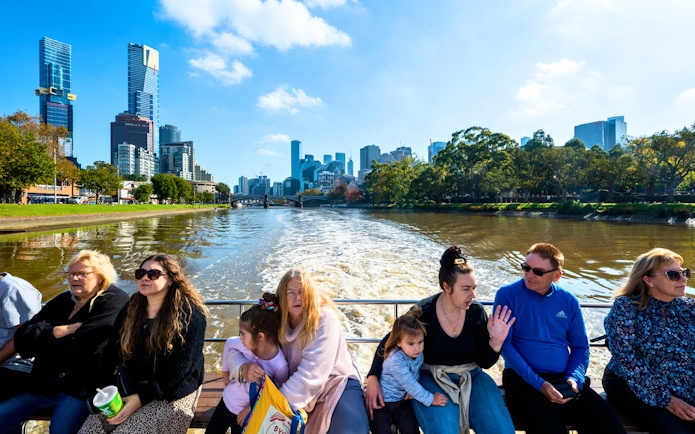 People enjoying a Yarra River cruise with Melbourne skyline in the background.