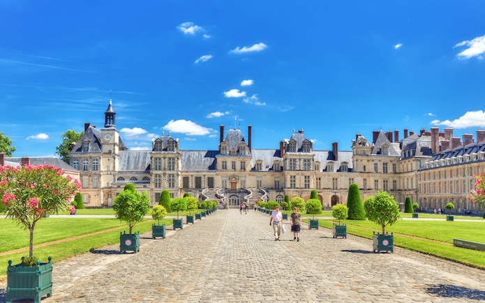 Palace of Fontainebleau courtyard with visitors walking on cobblestone path.