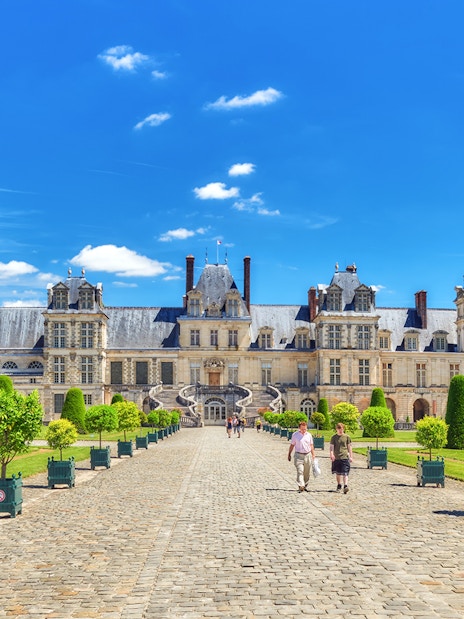 Palace of Fontainebleau courtyard with visitors walking on cobblestone path.