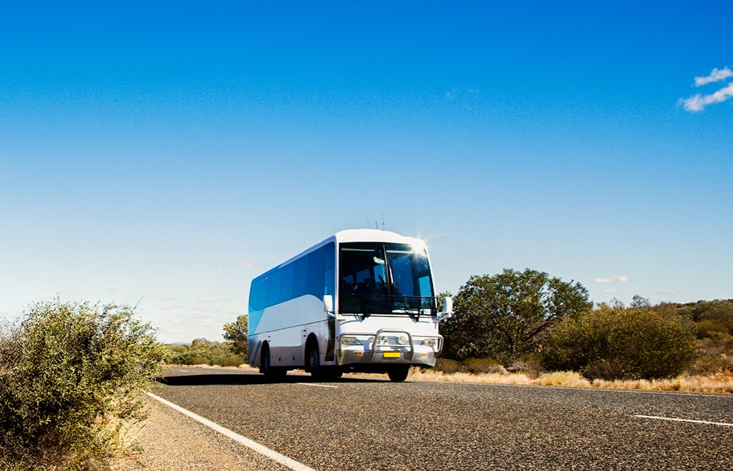 Bus traveling on a scenic road in Australia with lush greenery and clear skies.