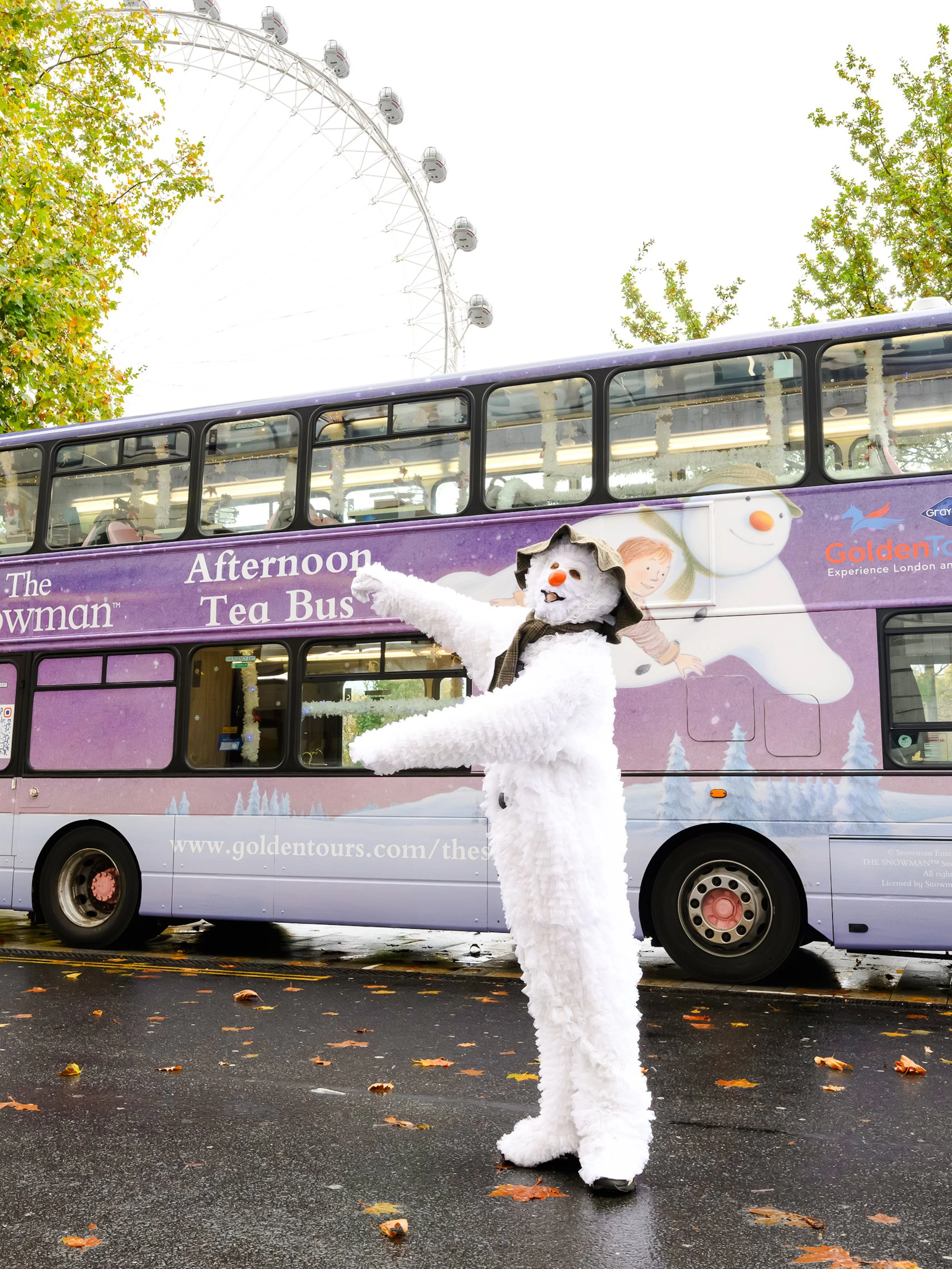 Snowman character in front of The Snowman™ Afternoon Tea Bus in London.