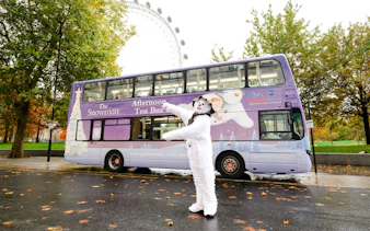 Snowman character in front of The Snowman™ Afternoon Tea Bus in London.