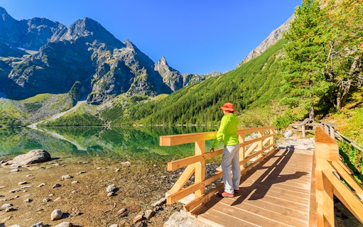 Woman on a wooden bridge overlooking Morskie Oko lake in Tatra Mountains, summer.