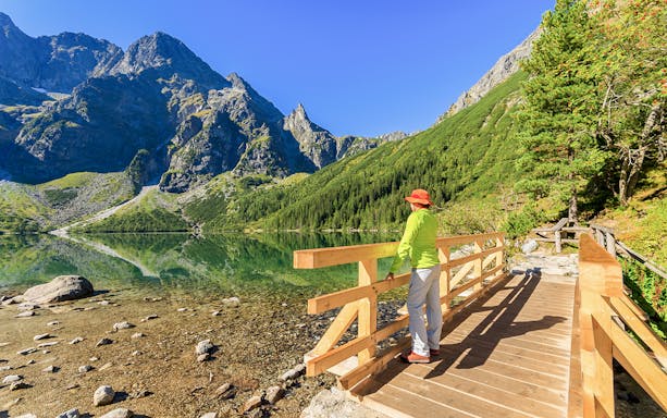 Woman on a wooden bridge overlooking Morskie Oko lake in Tatra Mountains, summer.