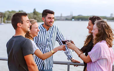 Group enjoying wine on Bateaux Bordelais Cruise with Bordeaux skyline in background.