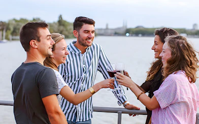 Group enjoying wine on Bateaux Bordelais Cruise with Bordeaux skyline in background.