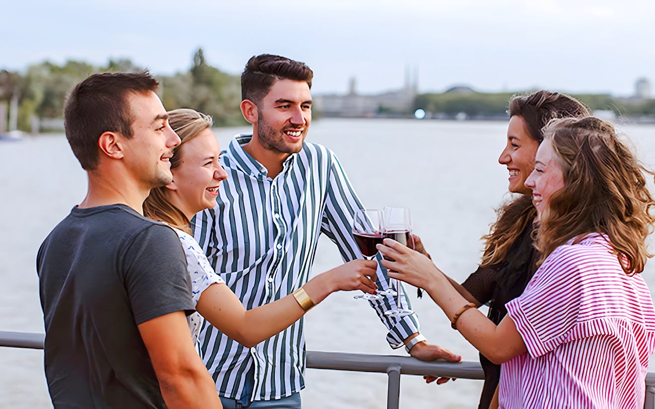 Group enjoying wine on Bateaux Bordelais Cruise with Bordeaux skyline in background.